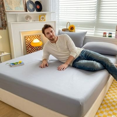 Drap housse gris clair jeune homme apprécie la douceur de son lit