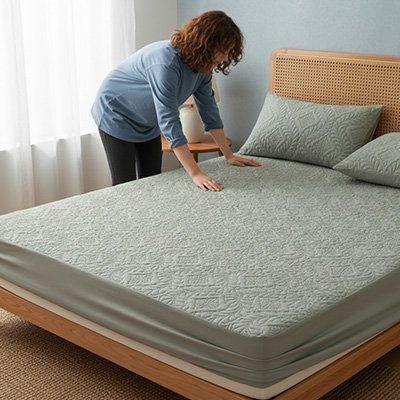 Protège matelas imperméable respirant gris avec une femme qui pose les mains sur un lit entièrement gris
