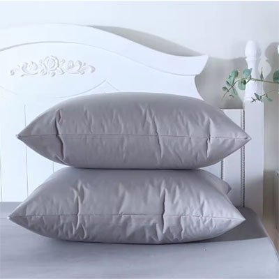 Taie d'oreiller premium confort gris avec deux  oreillers une par dessus l'autre devant tête de lit blanche