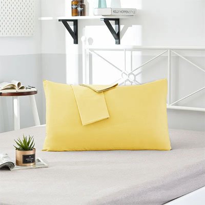 Taie d'oreiller douceur réparatrice jaune sur lit blanc avec tête de lit blanche entourée de jolis accessoires