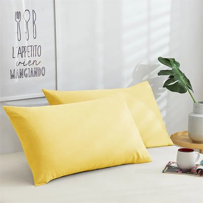 Taie d'oreiller douceur réparatrice jaune sur un lit blanc appuyée contre le mur sous un joli cadre