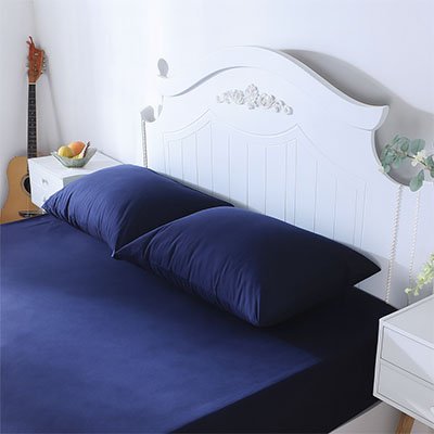 Taie d'oreiller premium confort bleu sur des draps bleus avec un lit et des tables de chevet blanches
