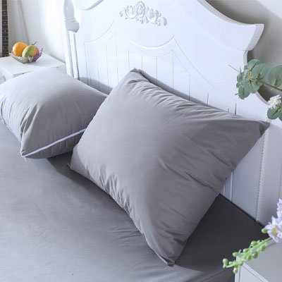 Taie d'oreiller premium confort gris avec vue rapprochée de deux oreillers appuyés contre une  tête de lit blanche